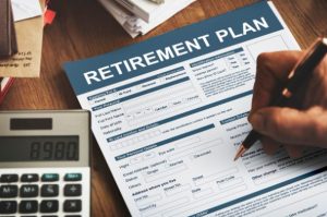 Person filling out a retirement plan form with a calculator on the desk, symbolizing financial preparation for retirement in the UK.
