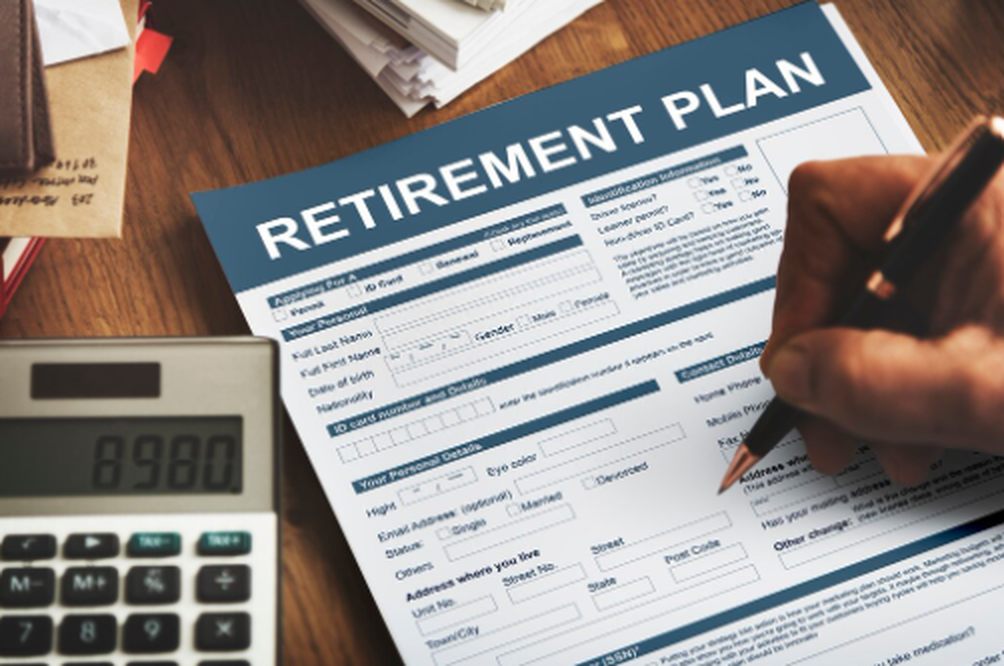 Person filling out a retirement plan form with a calculator on the desk, symbolizing financial preparation for retirement in the UK.