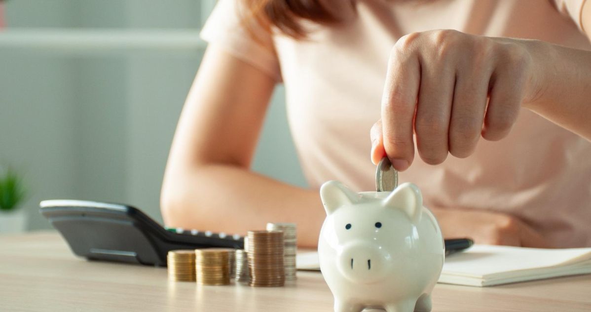 Person saving money by putting a coin into a white piggy bank, symbolizing financial planning and tax-free growth with Individual Savings Accounts.