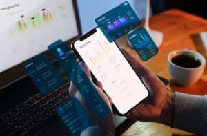 Person using a smartphone with finance apps on screen, analysing charts and digital tools to better manage personal finances at home.