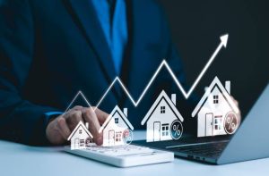 A businessman uses a calculator and laptop with a digital graphic showing house icons, percentage signs, and an upward arrow representing a rent increase and rising property costs in major cities.